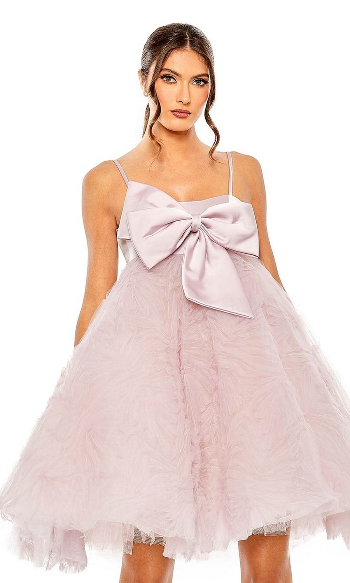 A woman models the Mac Duggal Short Homecoming Dress 20583 in rose pink, featuring a large bow front, sleeveless thin straps, and a voluminous textured skirt. Her long brown hair flows in loose waves.
